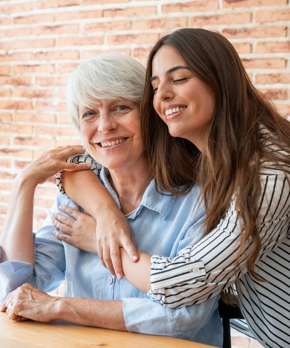 Caregiver embracing senior at table brick wall